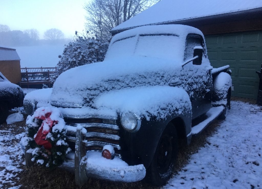 Black 1950 Chevy pickup truck in the snow with a red wreath on the front grill