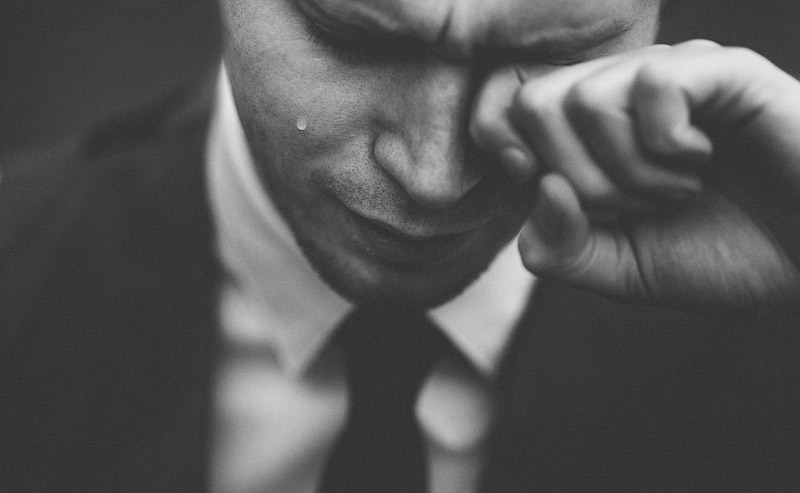 Black and white photo of businessman in suit artfully crying a single tear
