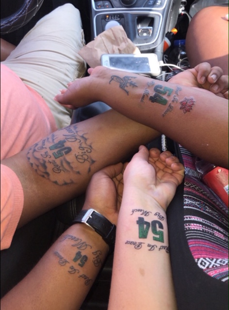 Four people's arms with memorials tattooed featuring 54 prominently