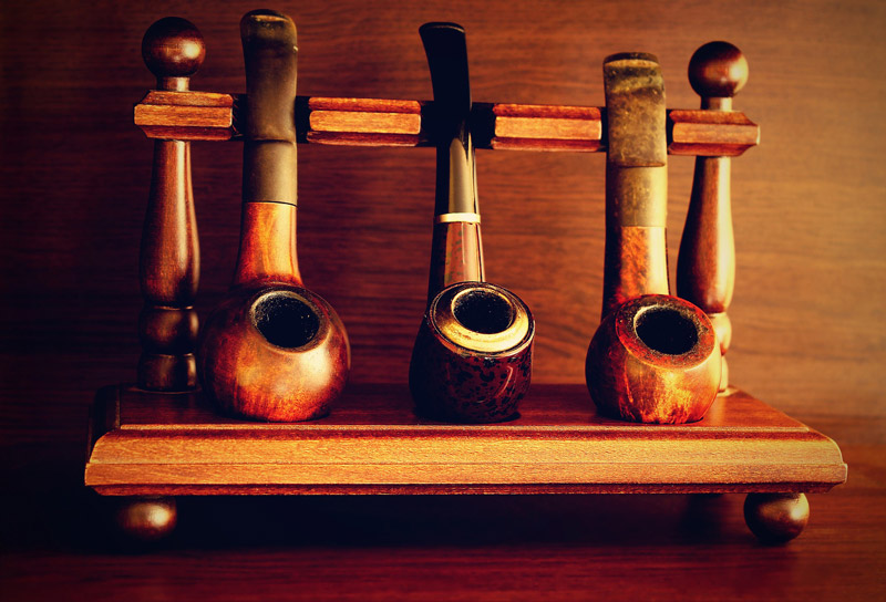Photo of wooden rack holding three old timey tobacco pipes